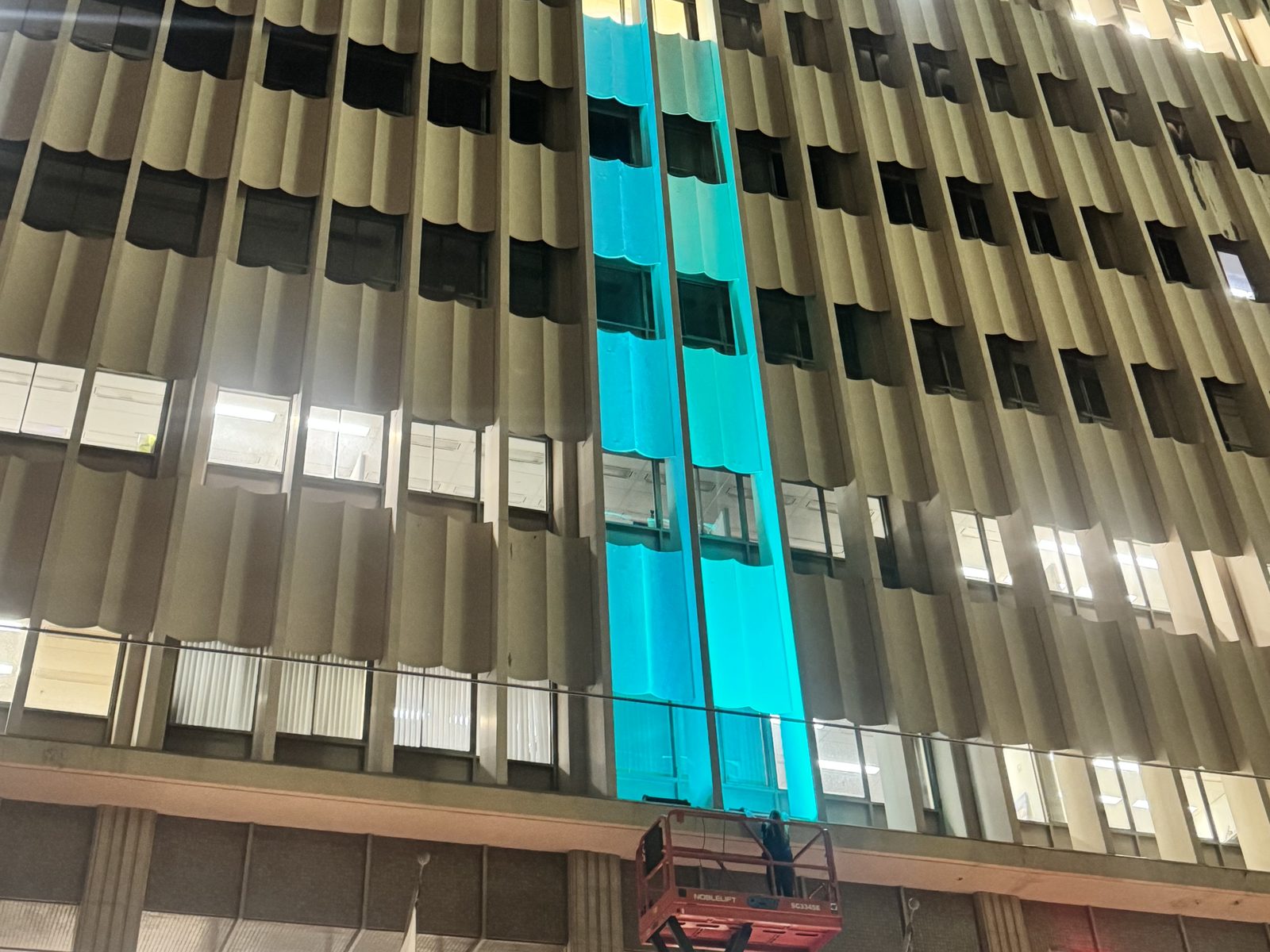 The same City Hall facade bay grazed cyan during the on-site mockup, seen from the plaza below